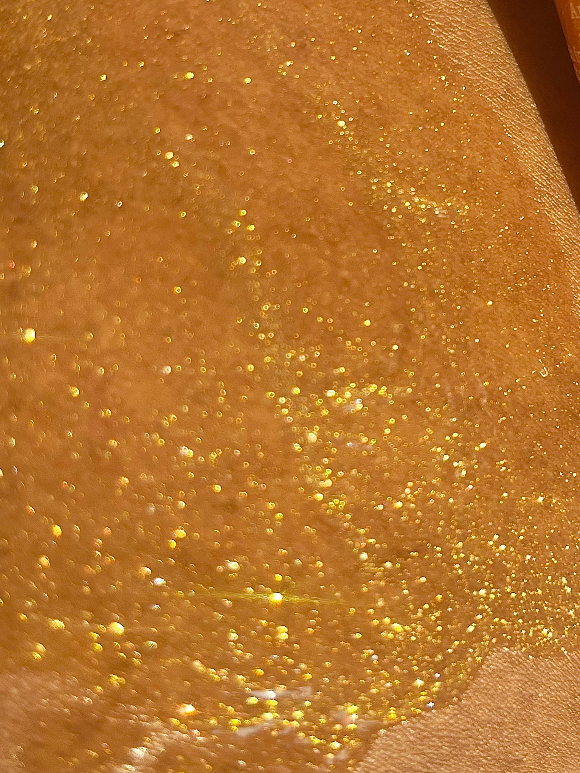 Close-up of gold glittery body oil serum texture