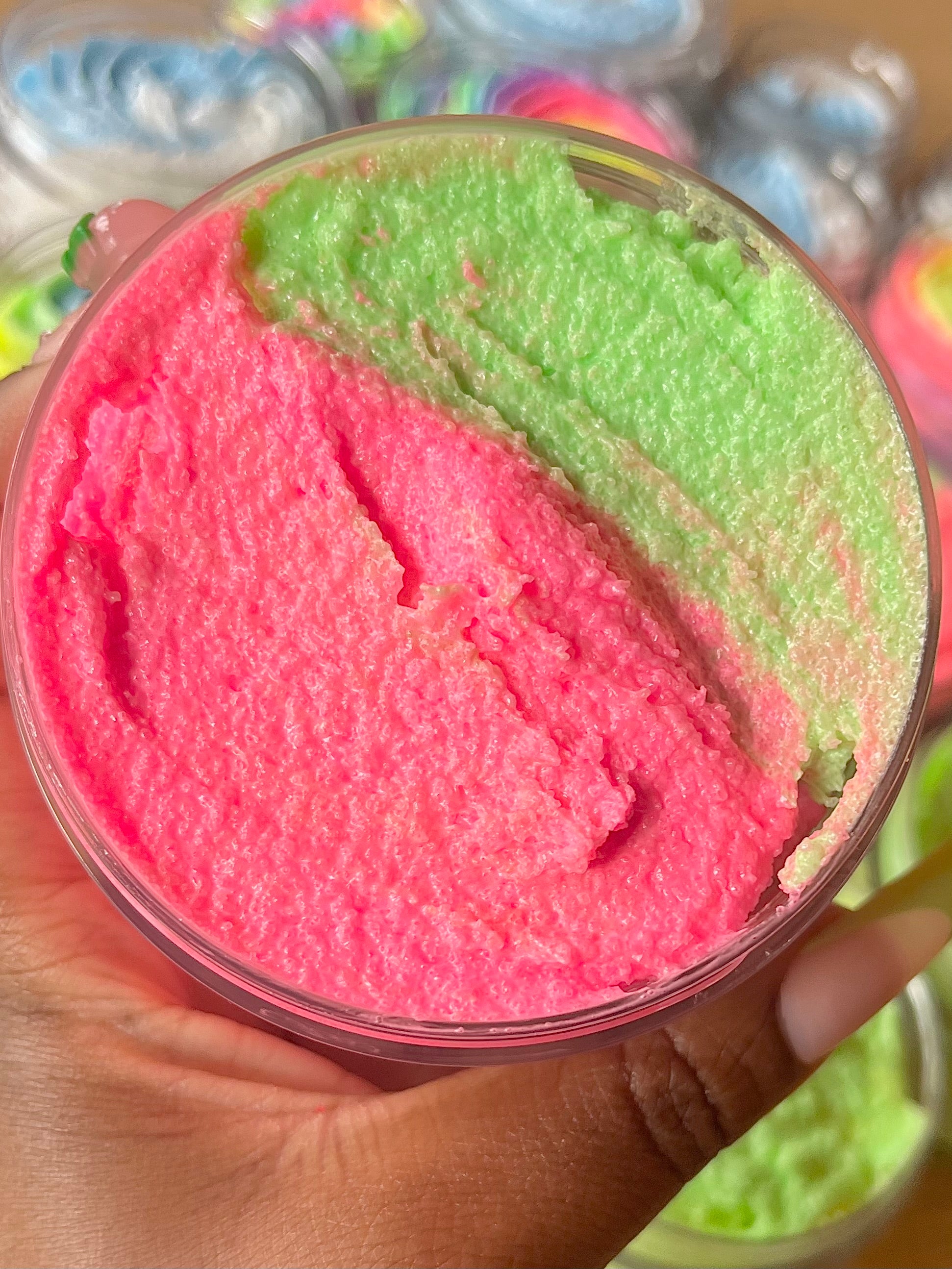 pink and green texture watermelon body scrub, summer fruit body exfoliant held by hand. A foaming/cleansing and exfoliating gentle body scrub to achieve smooth soft skin. UK handmade Vegan skincare that brings a fun luxurious experience to self care and shower routines. Scrub and get rid of patchy dry skin, clogged pores and ingrown hairs. The best body scrub you could ever ask for.