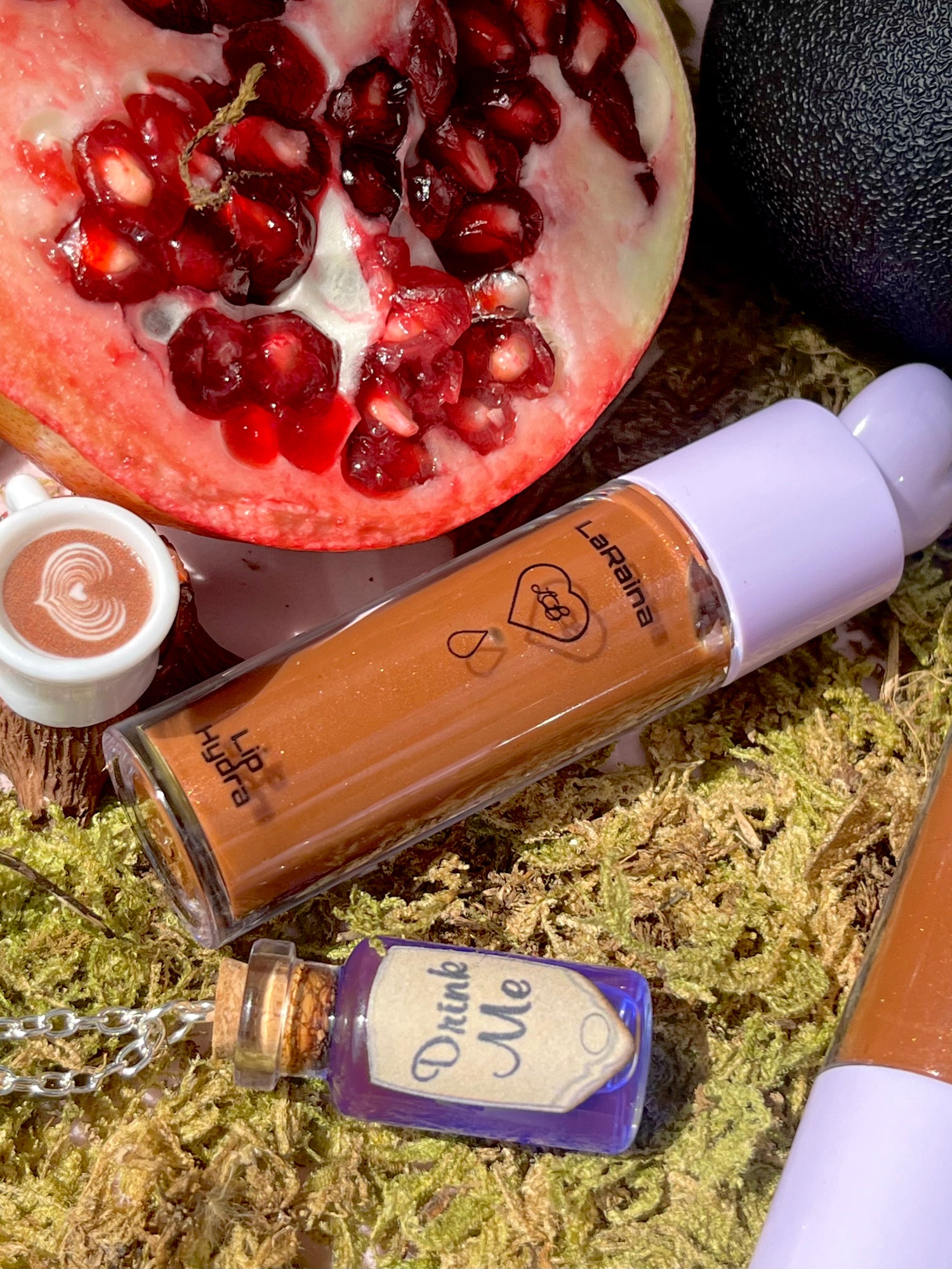 Makeup product with a pomegranate and 'Drink Me' bottle on a textured surface
