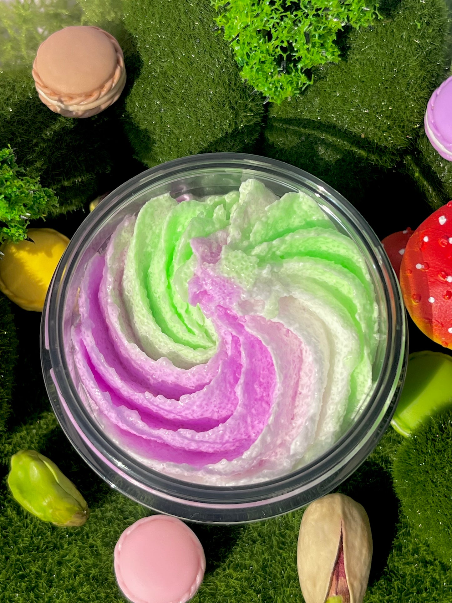 Colorful whipped cream in a container surrounded by greenery and pastel-colored macarons.