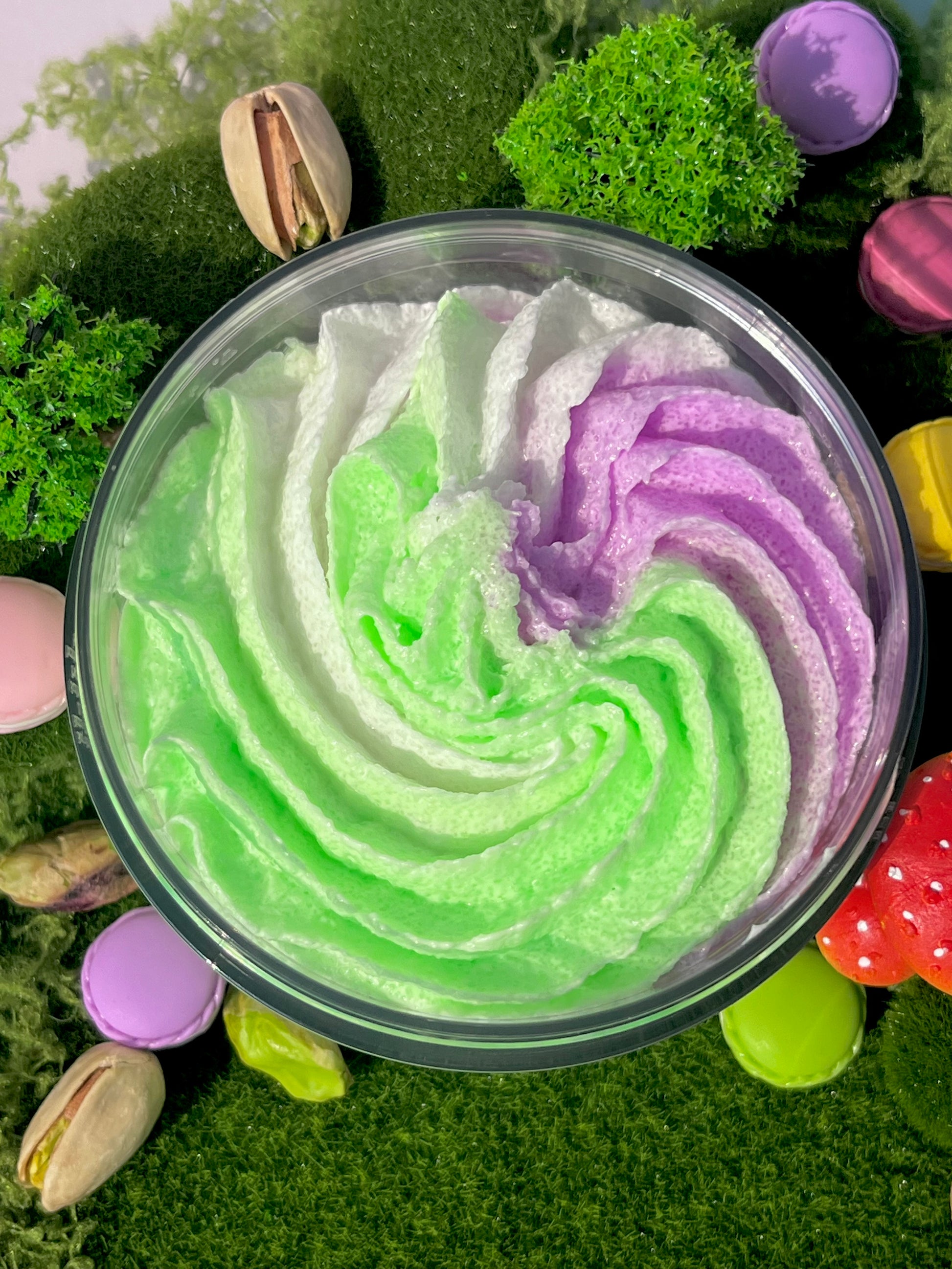 Colorful whipped cream swirl in a container with green and purple layers, surrounded by pistachios and cookies.